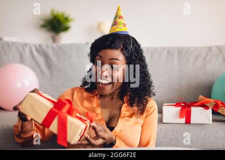 Excited Black Woman Opening Wrapped Birthday Gift Box At Home Stock Photo