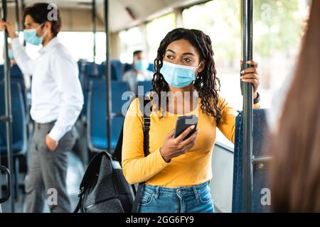 Beautiful black woman in face mask using phone in bus Stock Photo