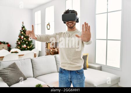 Young hispanic man smiling happy using 3d vr glasses at home. Stock Photo
