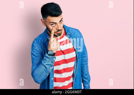 Young hispanic man with beard wearing casual denim jacket pointing to the eye watching you gesture, suspicious expression Stock Photo
