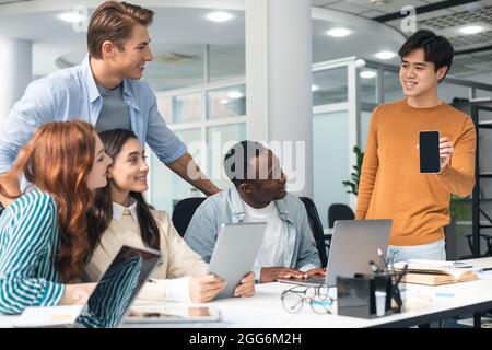Asian guy showing phone with blank space to coworkers Stock Photo
