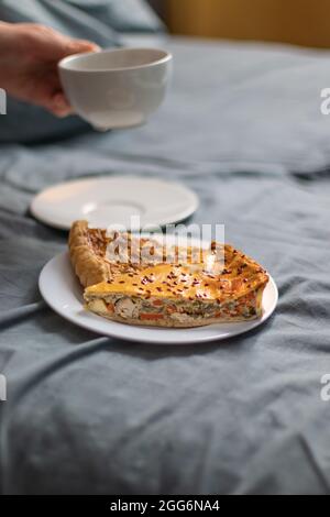 Two slices of homemade quiche pie on a white plate and a cup of aromatic chamericano coffee on the bed at home Stock Photo