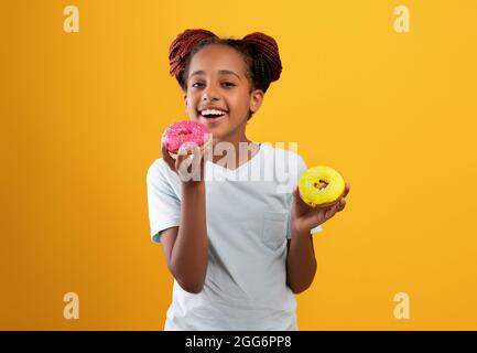 Pretty black girl holding colorful donuts, isolated on yellow background Stock Photo