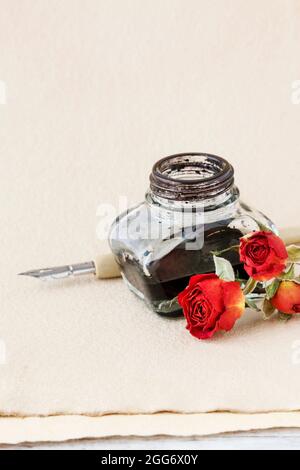 Inkwell, pen and dried roses on vintage paper background. Copy space. Stock Photo