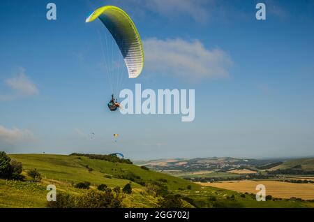 Firle, Lewes, East Sussex, UK. 29th Aug, 2021. Morning mist clearing with wind from the North brings paraglider pilots to the glorious South Downs. Pilots fly over the rural scene, Lewes in distance. Credit: David Burr/Alamy Live News Stock Photo