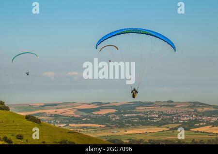 Firle, Lewes, East Sussex, UK. 29th Aug, 2021. Morning mist clearing with wind from the North brings paraglider pilots to the glorious South Downs. Pilots fly over the rural scene, Lewes town in distance. Credit: David Burr/Alamy Live News Stock Photo