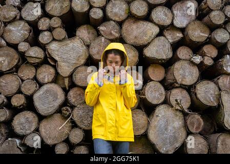 Woman wearing a yellow coat with hood, cut log background. Stock Photo