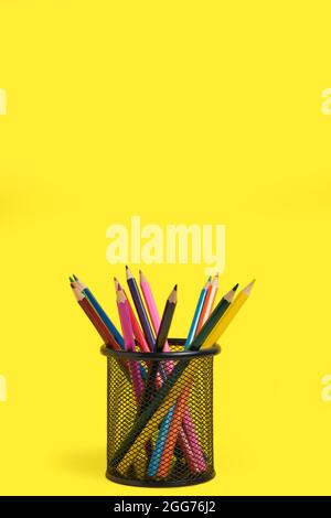 Office basket with colored pencils on yellow background Stock Photo