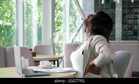 African-American lady types on laptop reading papers in cafe Stock Photo