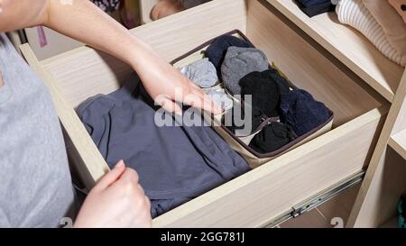 Woman chooses socks in drawer of large cabinet in room Stock Photo