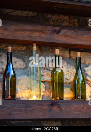 A variety of bottles stand on a wooden shelf against the background of a stone wall. Stock Photo