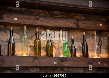 A variety of bottles stand on a wooden shelf against the background of a stone wall. Stock Photo