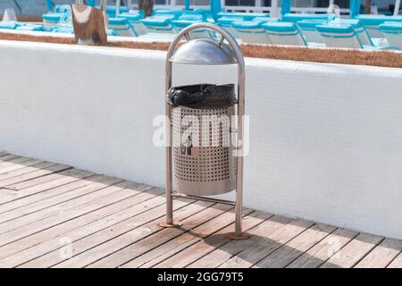 Metal trash bin with an office bag on the waterfront near the hotel. Global pollution concept. Clean city street with a place for garbage containers. Stock Photo
