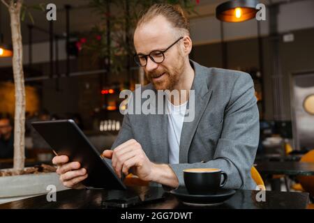 Confident middle aged white businessman using digital notepad while sitting in the cafe indoors Stock Photo