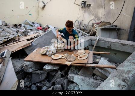 A boy sorting out food. Palestinians inspect the damage at a destroyed house that was hit by an Israeli air strike in the southern Gaza Strip, amid the escalation of violence between Israel and Gaza in May 2021. Gaza Strip. Stock Photo