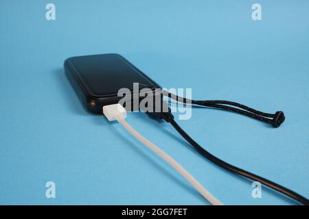 Black power bank with white and black wires on a blue background. Stock Photo