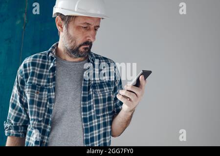 Construction engineer using smartphone on a morning break, relaxing and preparing for work Stock Photo