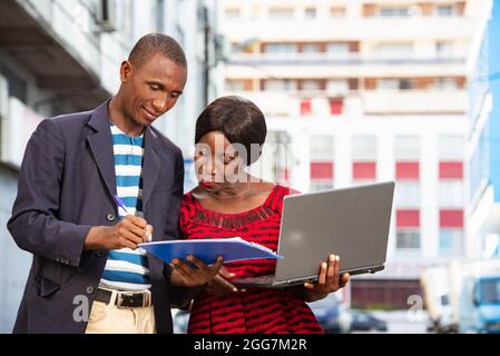 Confident african businessman pointing at a document explaining, the specific project has his assistant on the street while smiling Stock Photo