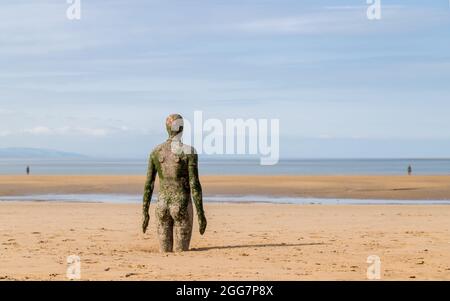 Three of the one hundred Iron Men figured known as Another Place pictured on Crosby beach near Liverpool in August 2021.  These statues were modeled o Stock Photo