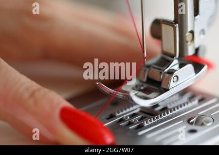 The womans hands are pulling a red thread in the sewing machine. Service and work on equipment in the studio Stock Photo