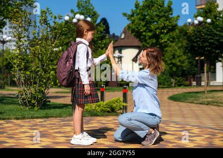 Caucasian schoolgirl with backpack and uniform says goodbye to her mother Stock Photo