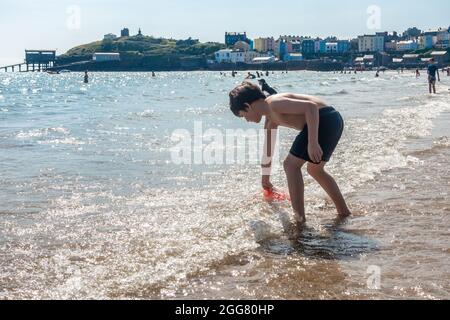 A young boy paddle on the North Beach at Tenby in Wales and collects sea water in a plastic bucket Stock Photo