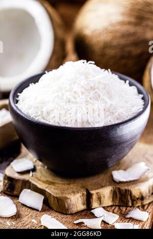 grated coconut inside a clay bowl, with coconut and coconut pieces in the background, culinary ingredient for sweets Stock Photo