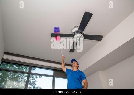 Man cleans dusty ceiling fan blades inside of a home Stock Photo