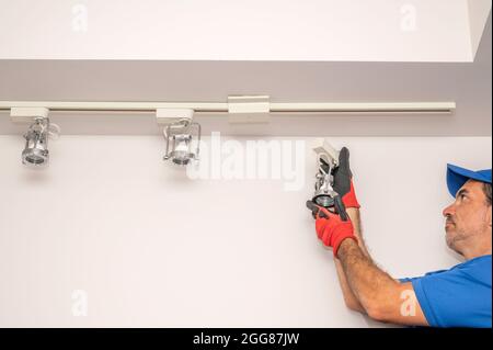 Electrician removing a track lighting fixture from the ceiling Stock Photo