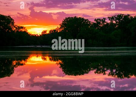 Shot of a lagoon during a sunset, mirroring the trees and sky in the water. Stock Photo