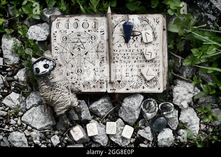 Grunge still life with voodoo doll, runes and witch book of magic spells. No foreign language, only fantasy symbols.  Esoteric, gothic and occult back Stock Photo