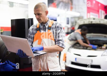 Mechanic man using laptop checking car in workshop Stock Photo
