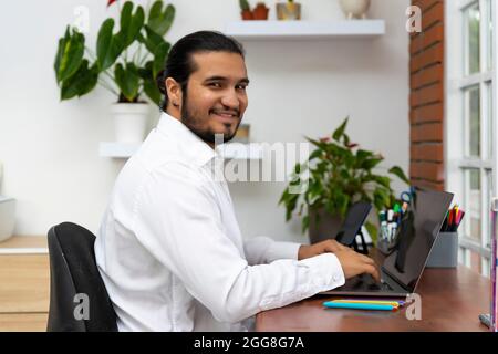 Young latina man using laptop and looking at camera Stock Photo