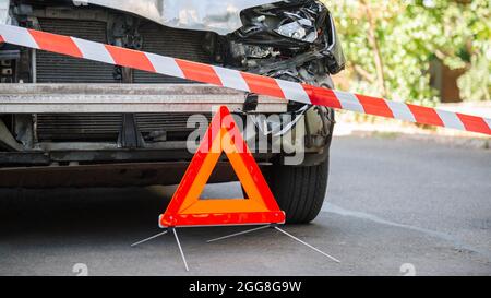 Destroyed car in car crash traffic accident on city road. Smashed broken car in accident. Red emergency stop triangle sign and Red warning police tape Stock Photo