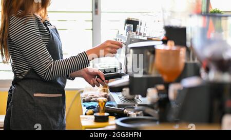 Cropped image of female barista making coffee by coffee machine, preparing tasty coffee for customer orders, brewing black coffee Stock Photo