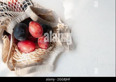Fresh plums with leaves on a reusable mesh shopping bag. Flat lay, autumn background. Ripe organic plums and nectarines in an eco string bag. Soft foc Stock Photo