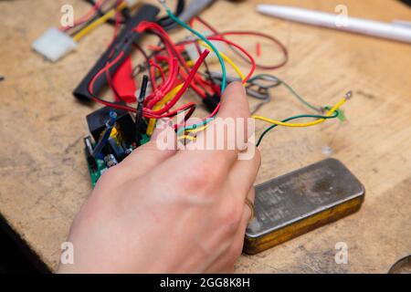 Young man's hands hold multicolored wires over desk with tools Stock Photo