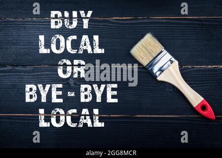 BUY LOCAL OR BYE - BYE LOCAL. Paint brush on a black wooden surface. Stock Photo
