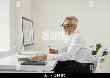Accountant or businessman sitting at office desk and working on laptop and desktop computers Stock Photo