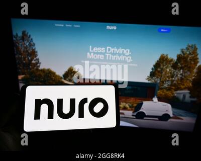 Person holding smartphone with logo of US robotics company Nuro Inc. on screen in front of website. Focus on phone display. Stock Photo