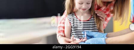 Doctor laboratory assistant taking blood of little girl using lancet in clinic Stock Photo