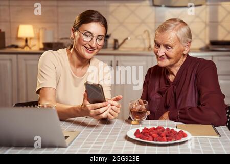 Happy woman showing photos on smartphone to senior person Stock Photo