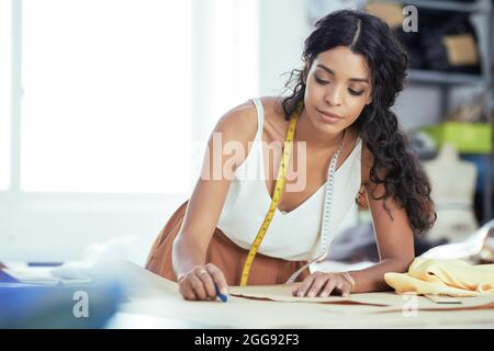 Pretty young seamstress taking notes on paper pattern of new dress she is working on Stock Photo