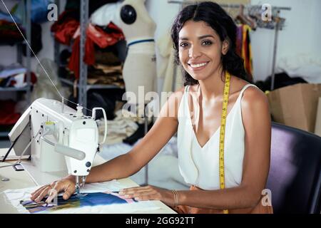 Portrait of beautiful smiling young seamstress working on sewing machine in her studio Stock Photo