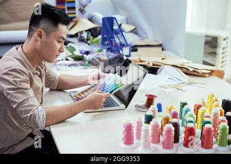 Young male fashion designer working at table in his studio and choosig colors from palette Stock Photo
