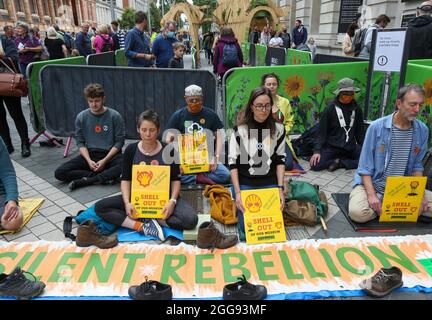 Protester seen participating in a silent rebellion sit-in protest outside as visitors go into the museum behind them .Protesters from Extinction Rebellion target the science museum on day 7 of the rebellion protests. They insist that the museum stop receiving money from multinational oil and gas company, Shell. They occupy the museum overnight, lock themselves onto railings inside and refuse to leave until the museum listen to their demands. The rebels also demand that government change policies to address the ecological and climate emergency and immediately stop all new fossil fuel investment Stock Photo