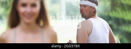 Fat man in sportswear looking at young girl jogging in park Stock Photo