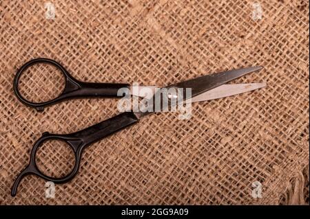 Small scissors on a piece of homespun fabric with a rough texture Stock Photo