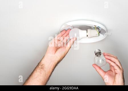 person replacing old incandescent light bulb with energy saving LED bulb in ceiling light, power saving concept Stock Photo