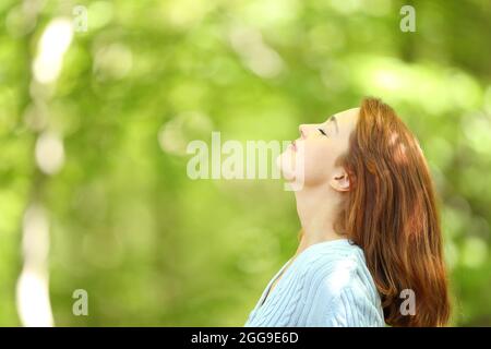 Side view portrait of a redhead woman breathing fresh air in a forest Stock Photo